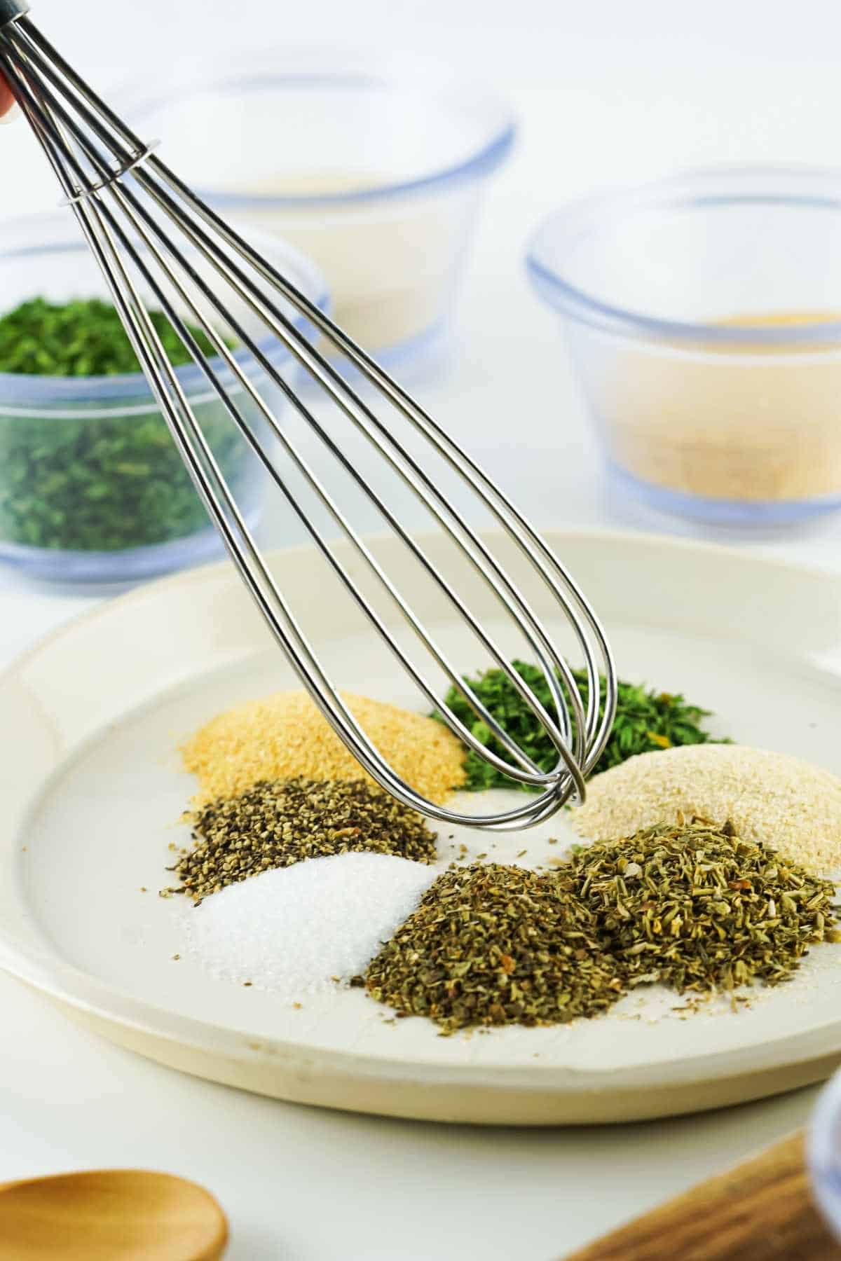 Whisk blending colorful green, yellow, and white spices in a shallow mixing bowl.