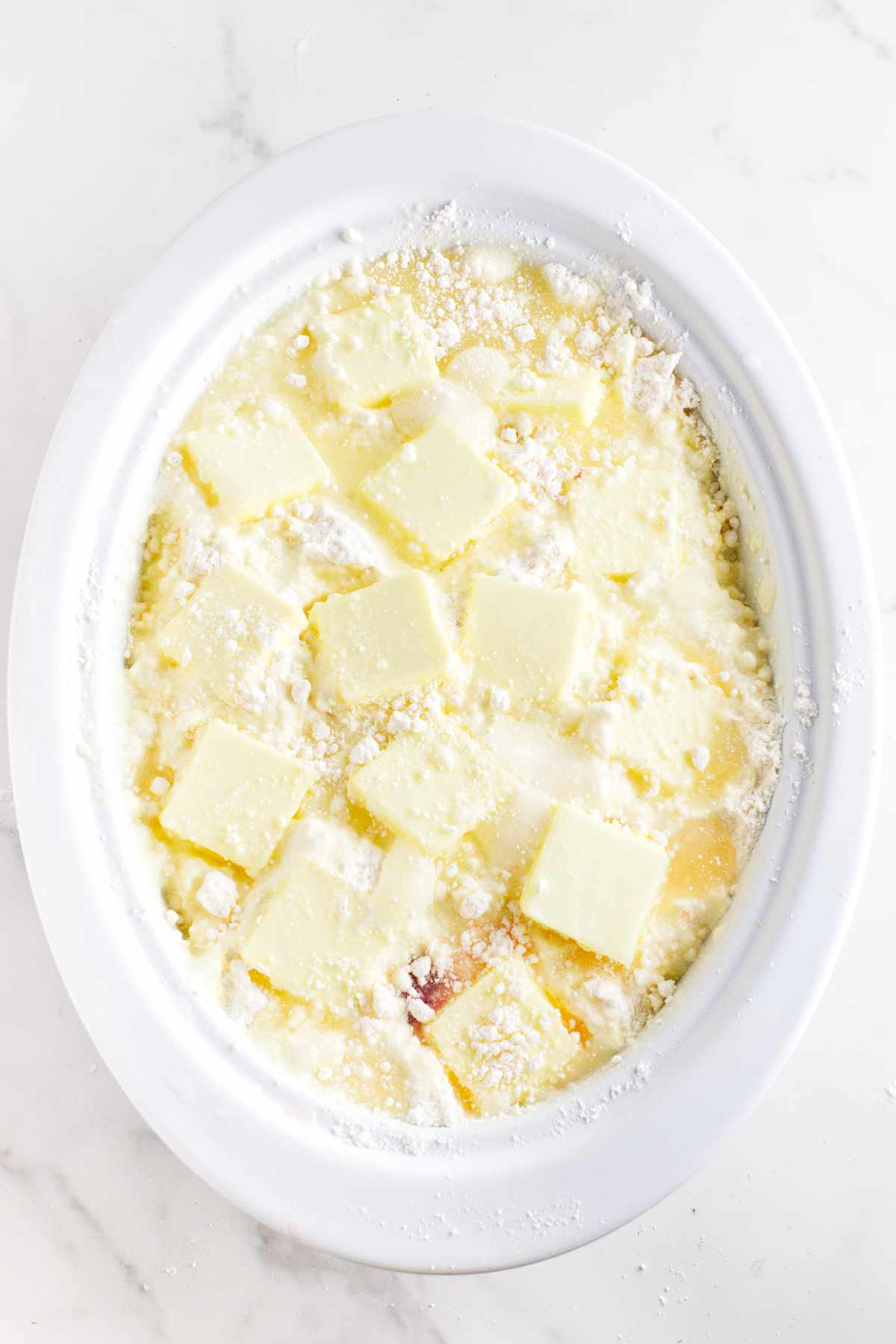 white oval casserole with white cake mix, pats of butter, and water on the top of the contents.