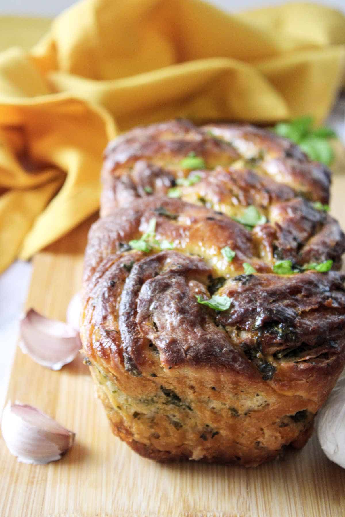 loaf of fresh baked twisted garlic bread on a wood cutting board.