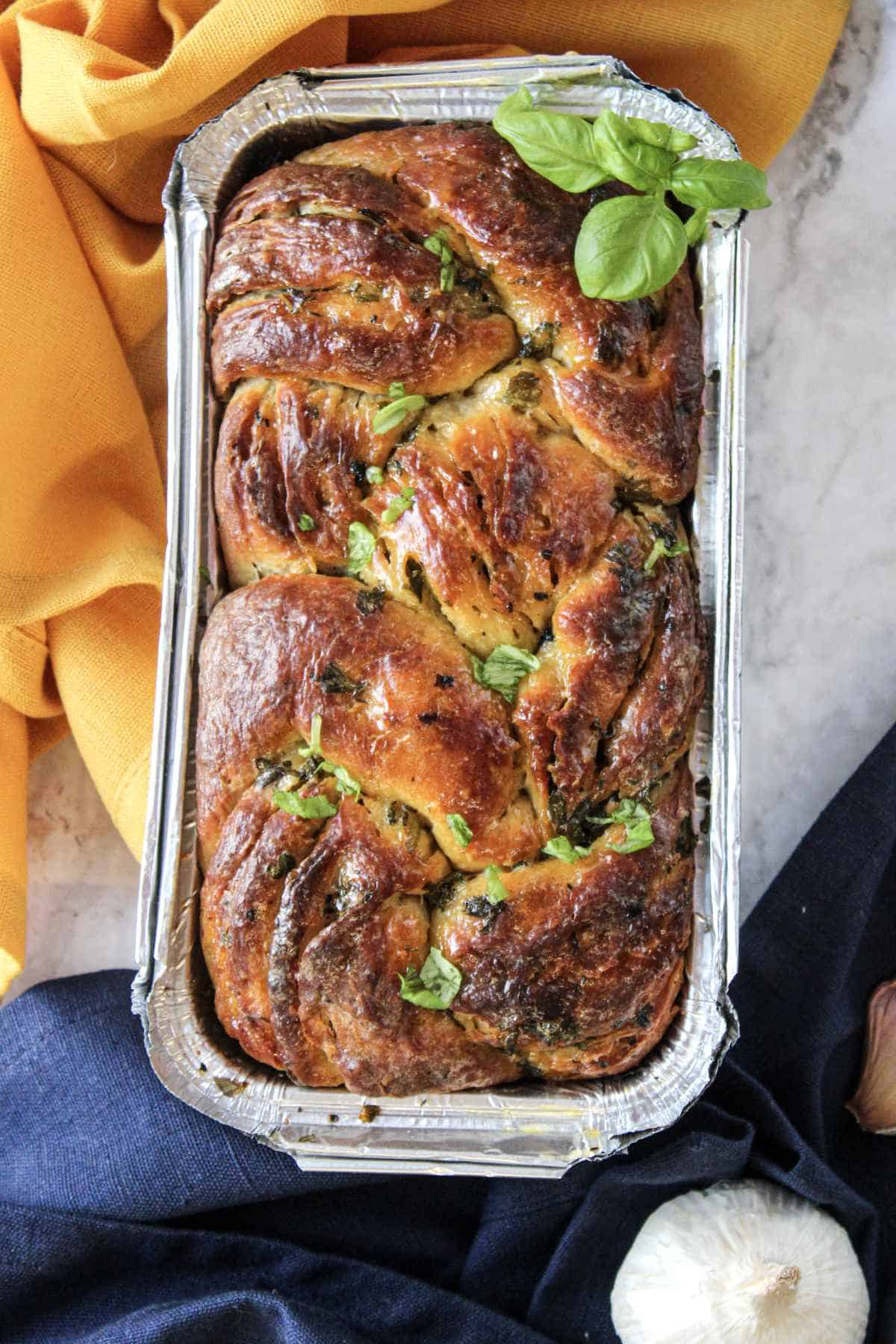 loaf of freshly baked twisted garlic bread in a pan on a counter.