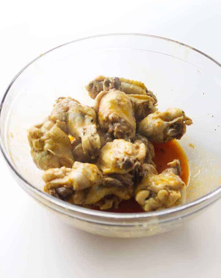 seasoning cooked chicken wings in buffalo sauce.