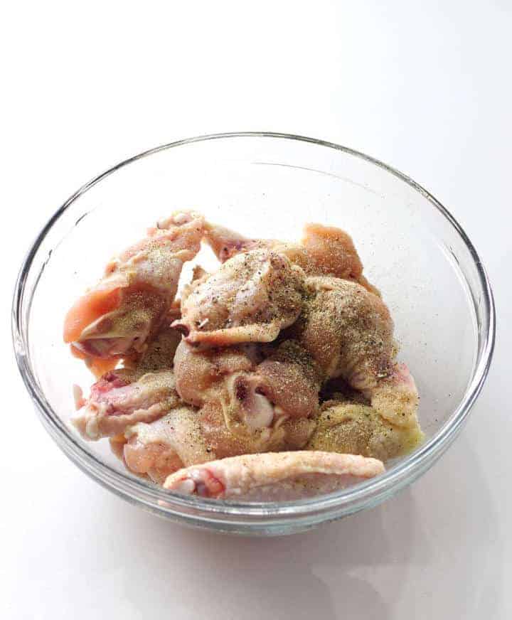 seasoning raw chicken wings in bowl.