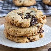 stack of four chocolate chip cookies on a white plate with cooking cookies on a rack in the background