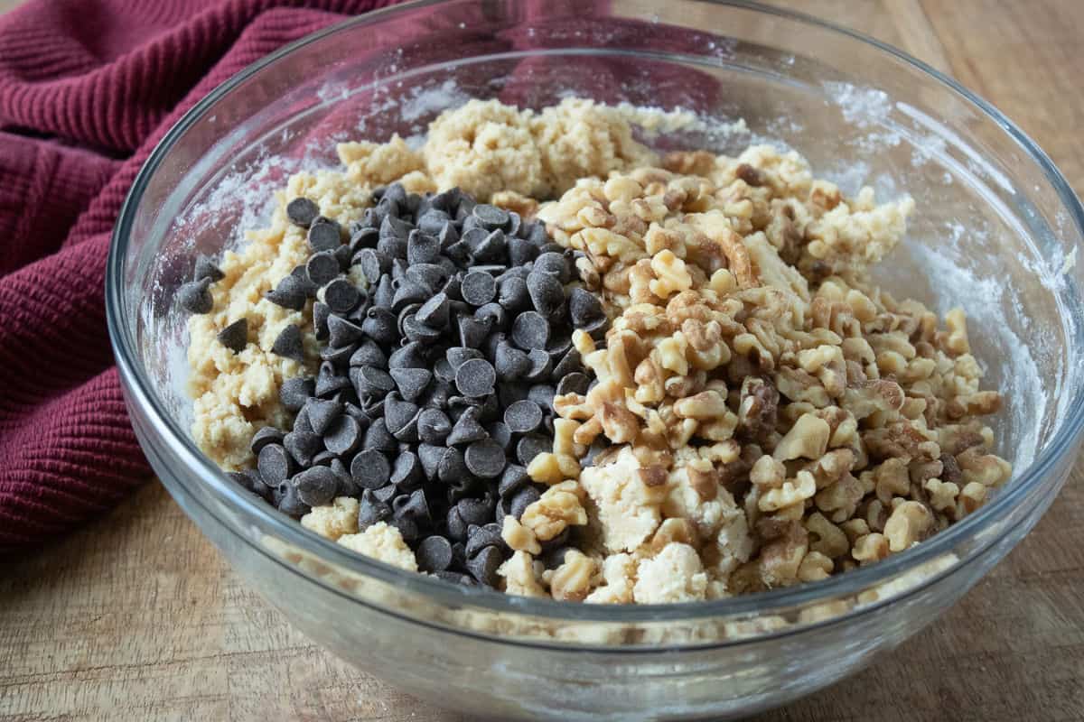 clear glass bowl of cookie batter with chopped walnuts and chocolate chips unmixed.