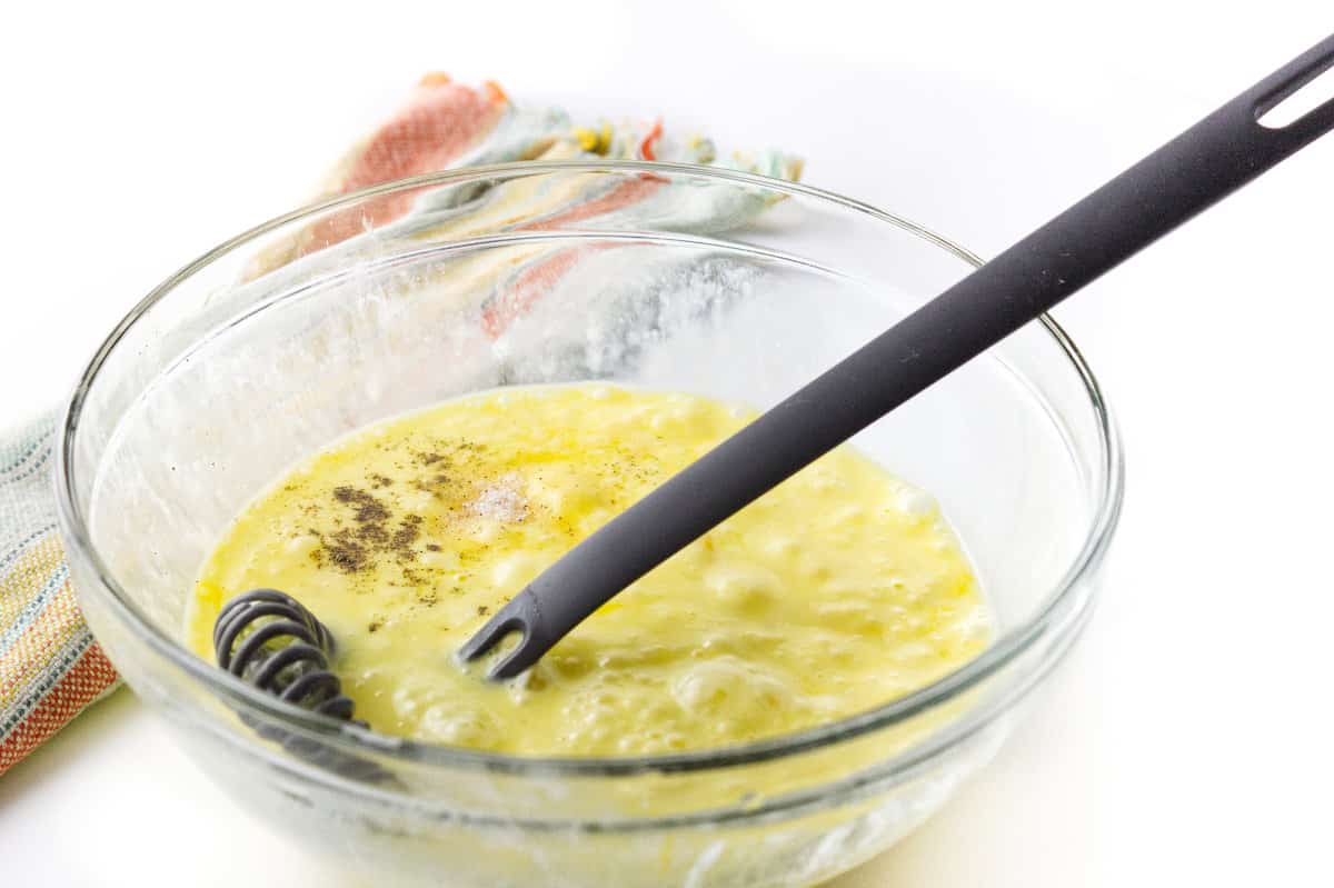 clear glass bowl with a swedish wisk in beaten eggs.