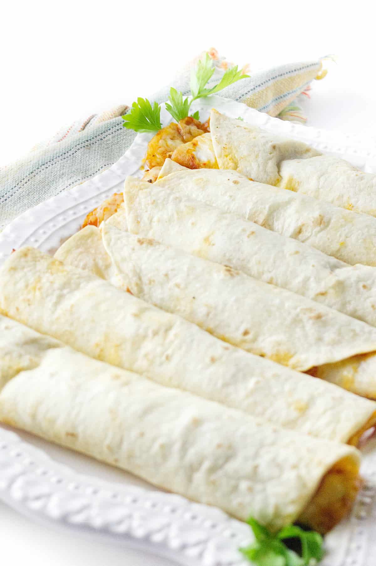 white platter of cooked breakfast flautas with parsley garnish ready for the buffet table.
