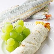 white plate with green grapes and one bacon cheese & egg breakfast flauta with napkin on a white background