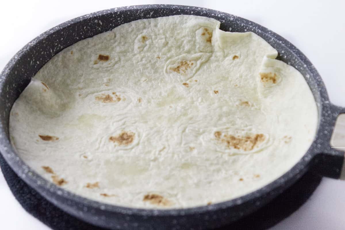 a flour tortilla placed on top of egg omlet in a skillet.