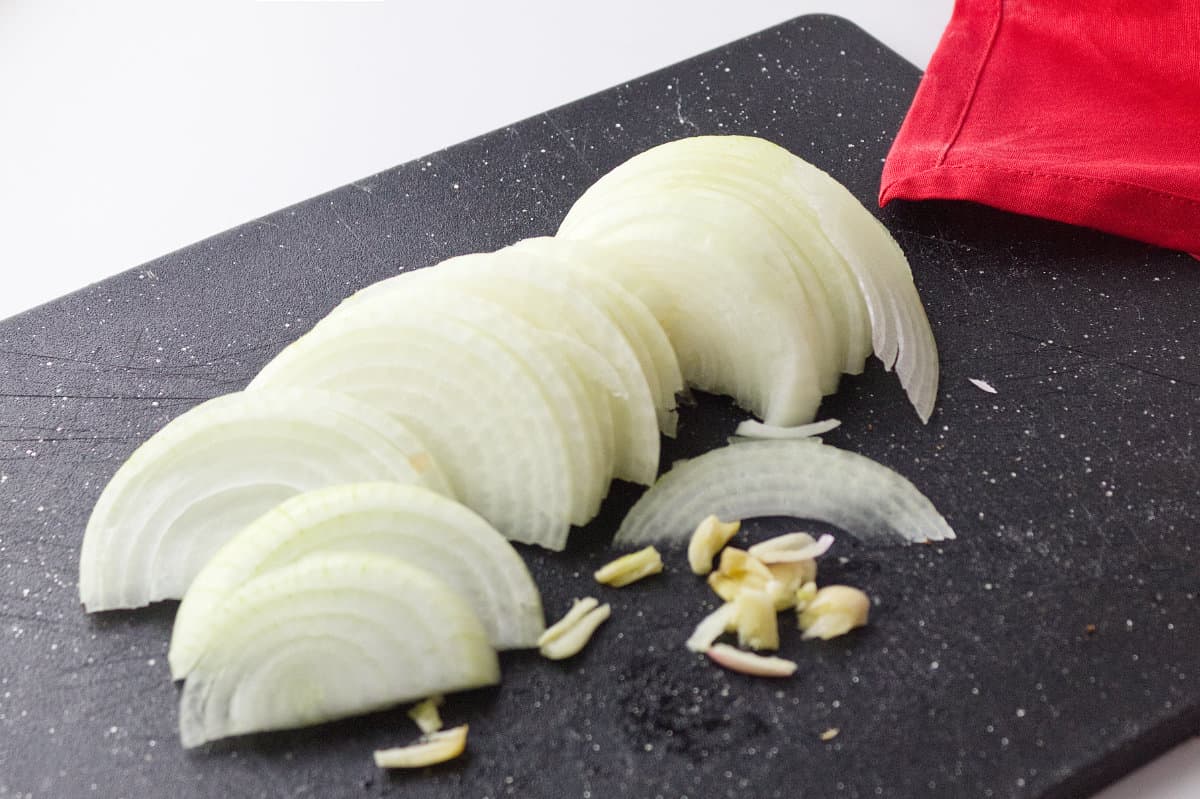 thin sliced onions and garlic on a black cutting board with a red napkin in background