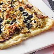 flatbread with carmelized onions, bacon, and olives on pizza stone and pot holder