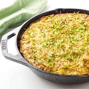 lodge cast iron skillet with grated potato kugel garnished with scallions