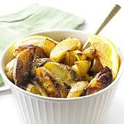 white casserole dish with roasted yukon potatoes with lemon and orange wedges with gold spoon and green napkin on a white background