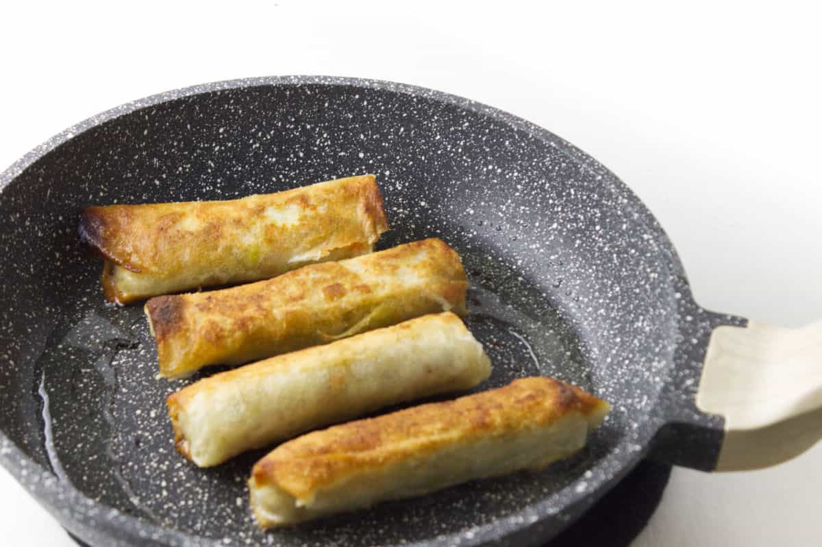 speckled granite skillet wtih four lumpia spring olls browning.