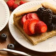 german puff pancake with sliced strawberries and blackberries on a white plate
