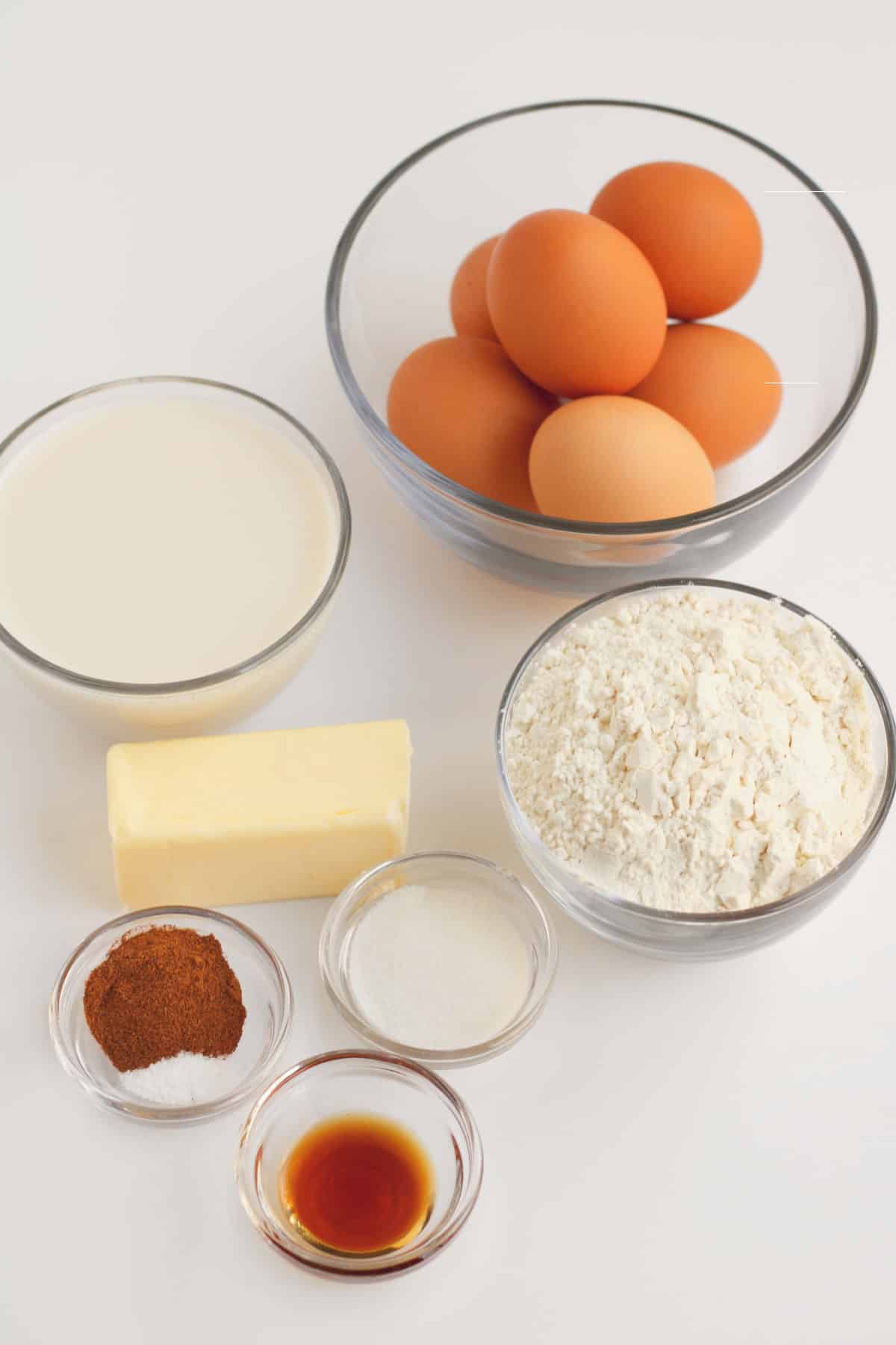 clear class bowls of eggs, milk, flour, cinnamon, vanilla, and a cube of butter