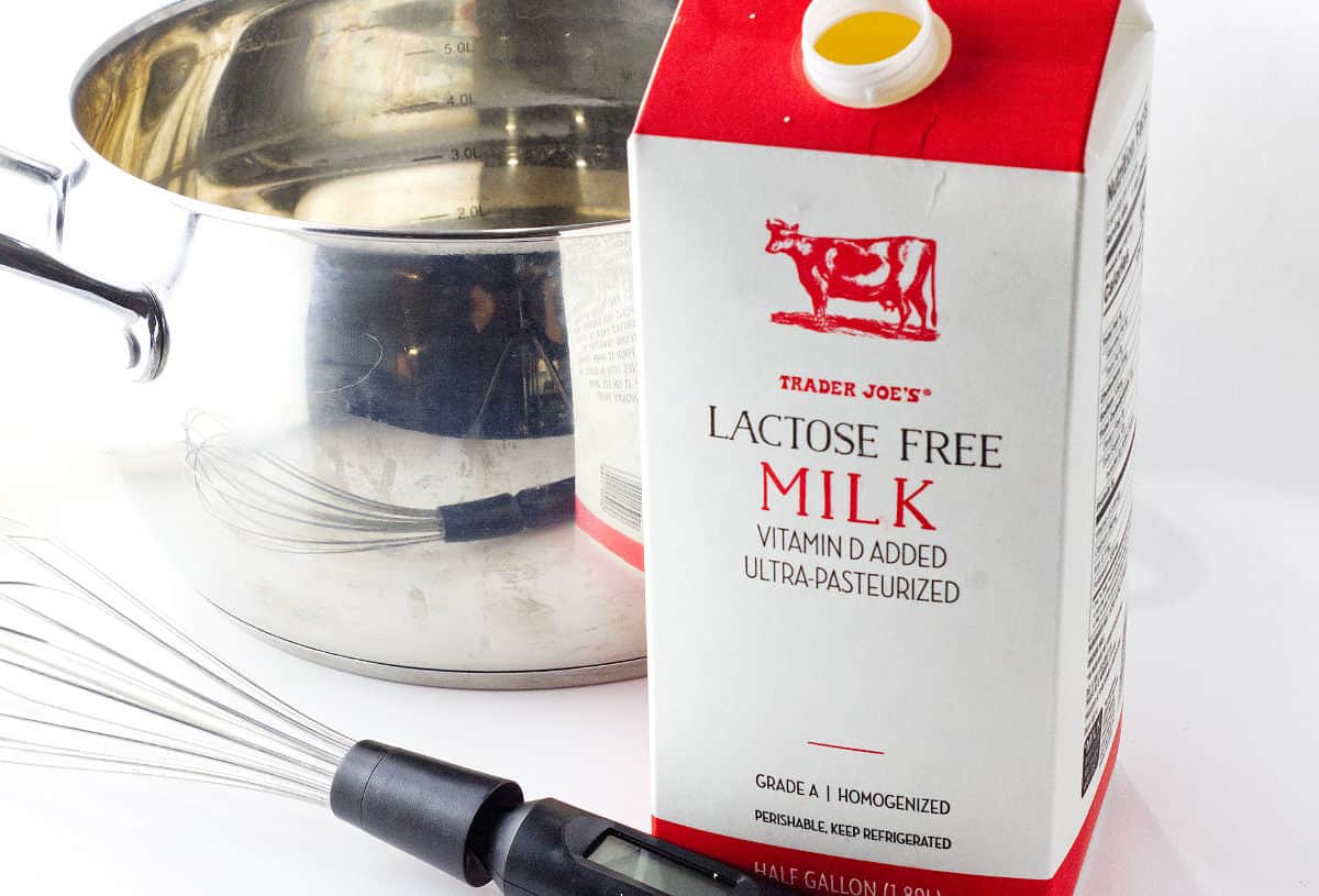 lactose free milk, stainless steel pot, and whisk on a white background