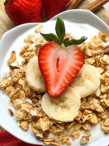 white lotus bowl full of lactose free yogurt with granola and sliced strawberries on a wood board
