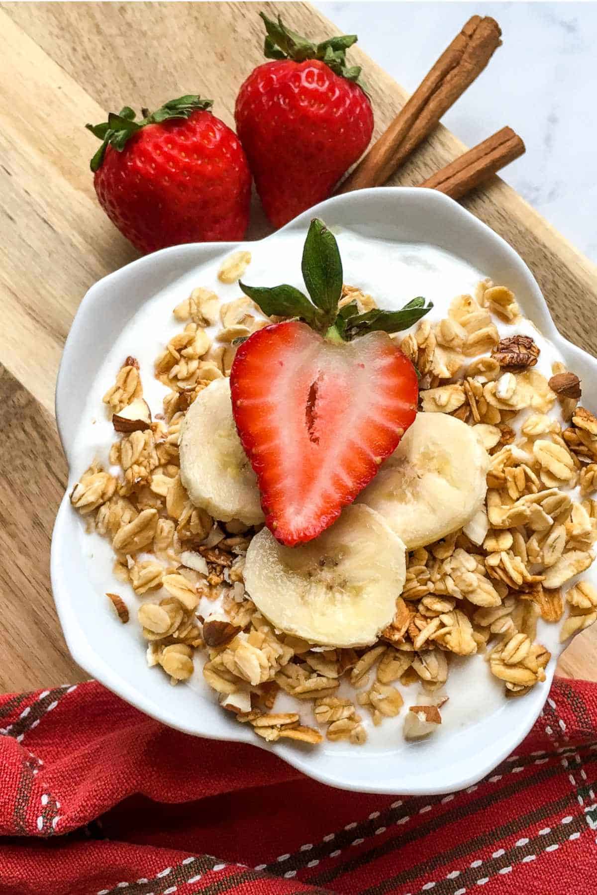 white lotus bowl full of lactose free yogurt with granola and sliced strawberries on a wood board