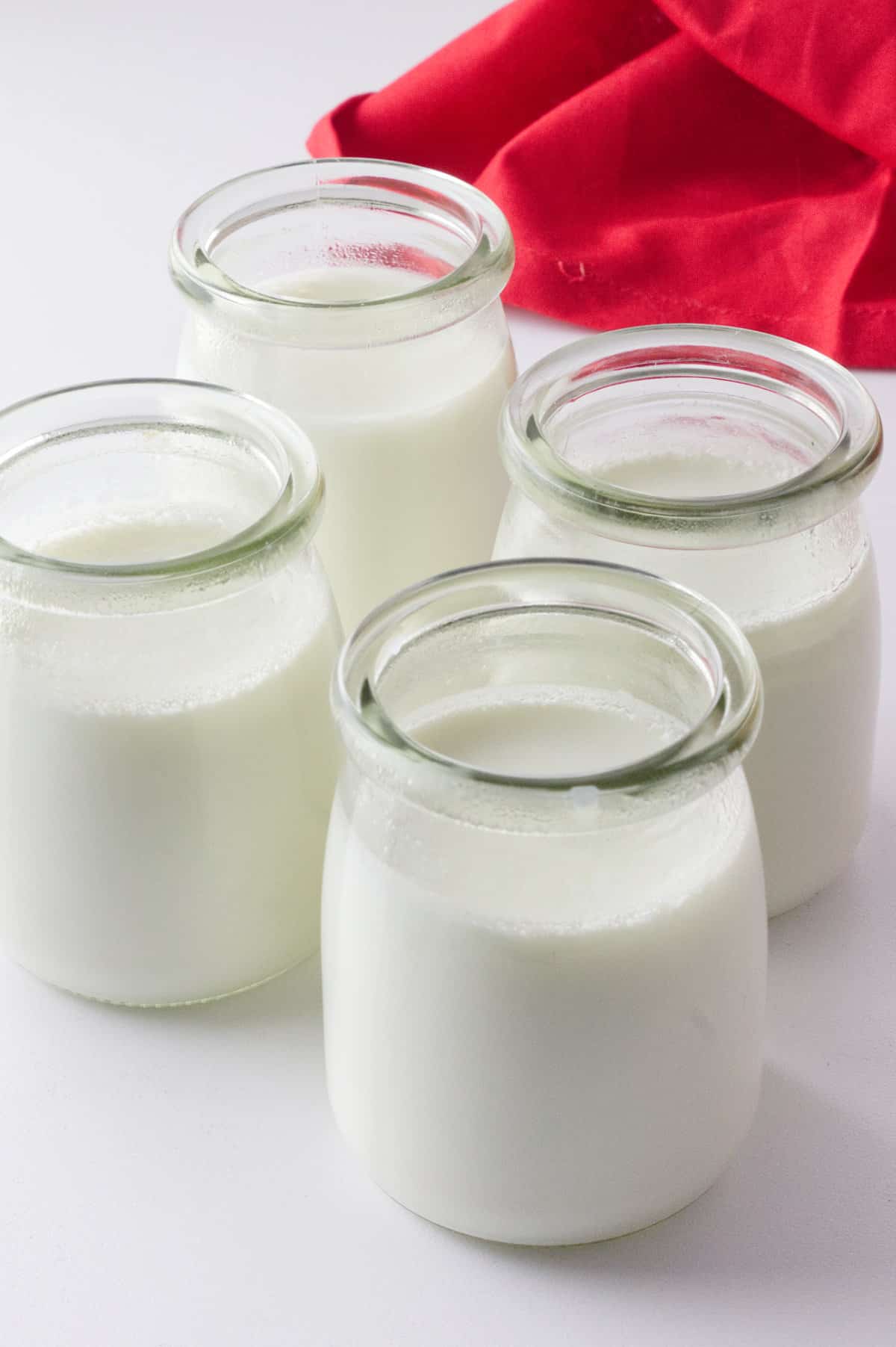 four clear glass jars of fermented milk on white background with red napkin.