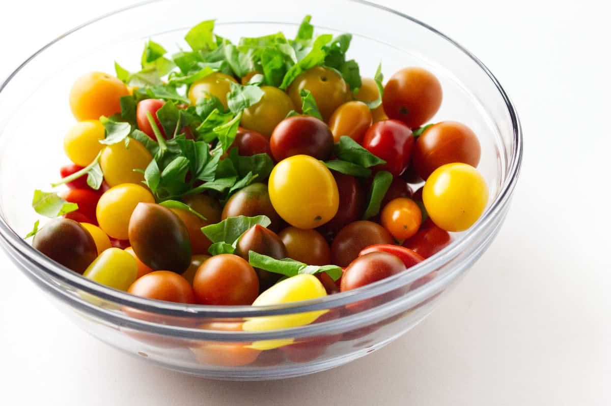 clear glass bowl of rainbow heirloom cherry tomatoes with minced basil.