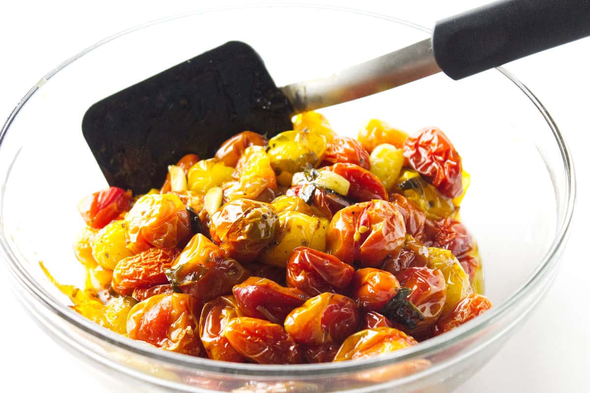 clear glass bowl of roasted heirloom cherry tomatoes with black spatula.