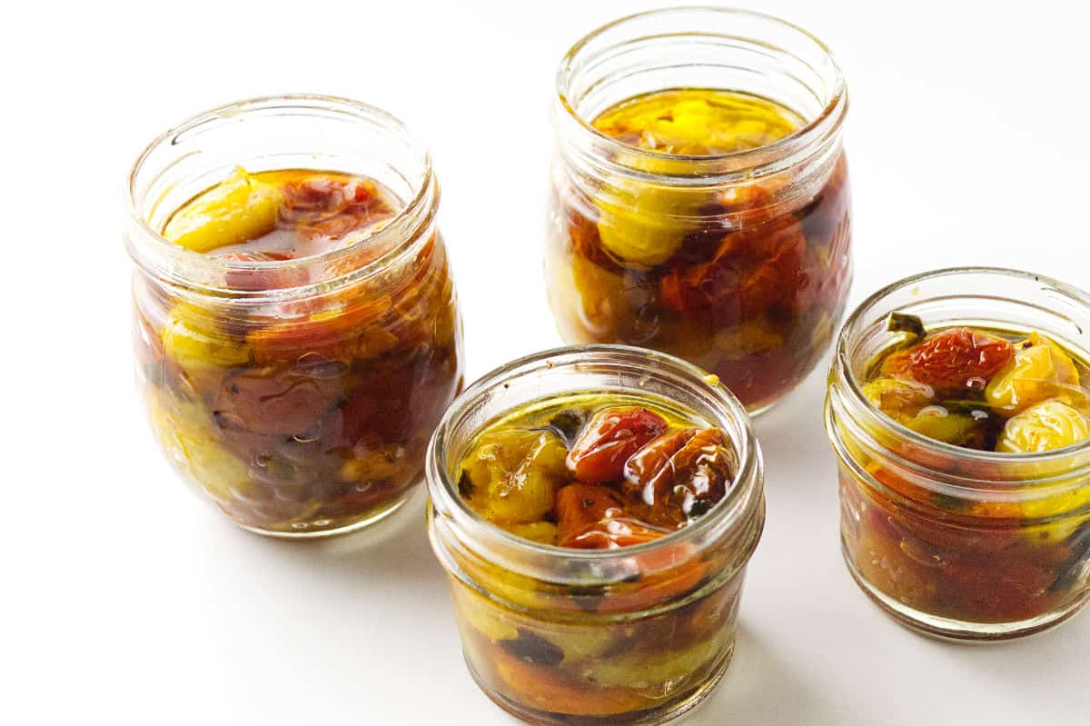 four ball canning jars filled with tomato confit and topped with olive oil and no lids.