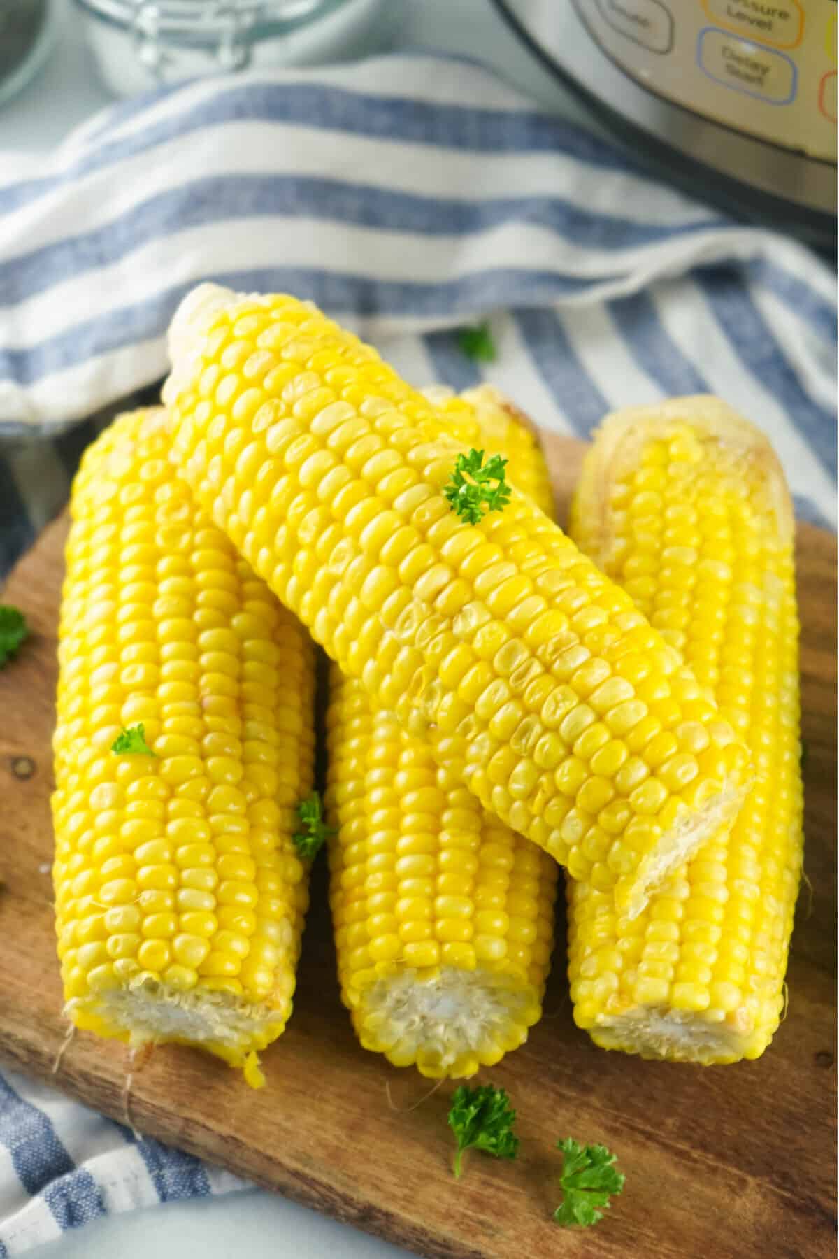 four cooked ears of corn on wood cutting board with parsley flakes.