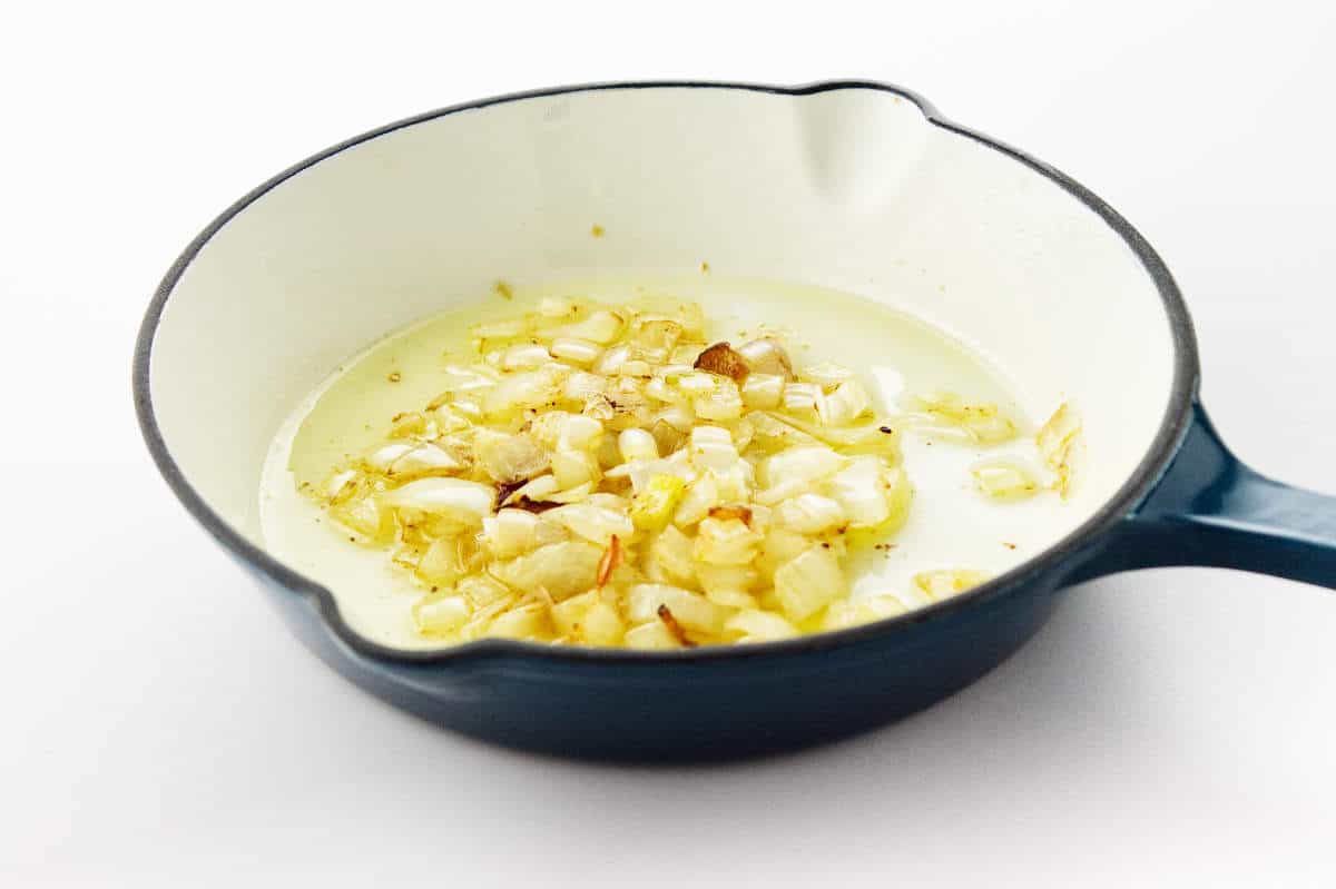 Golden onions sautéing in oil and Kentucky bourbon BBQ sauce in a blue-white enamel skillet on a white background.