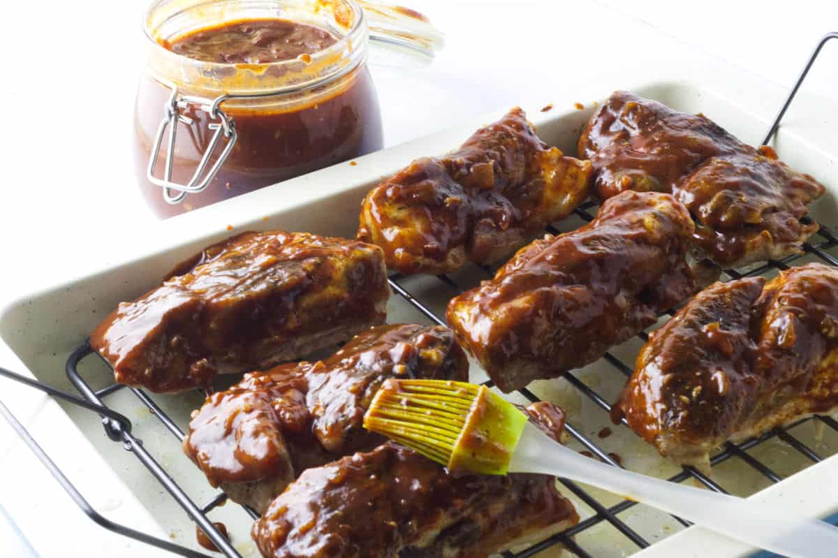 basting boneless pork ribs with barbecue sauce with jar of barbecue sauce in background.