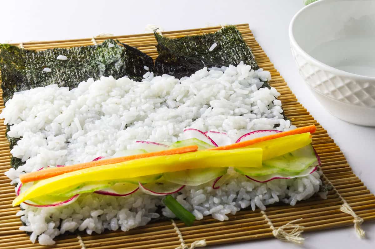 yellow radish, carrol, cucumber and rice spread out on black laver seaweed paper to make korean sushi roll.