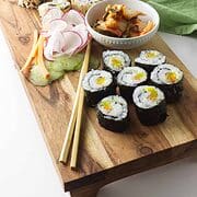 kimbap on a wood platter with chop sticks and kimchee.