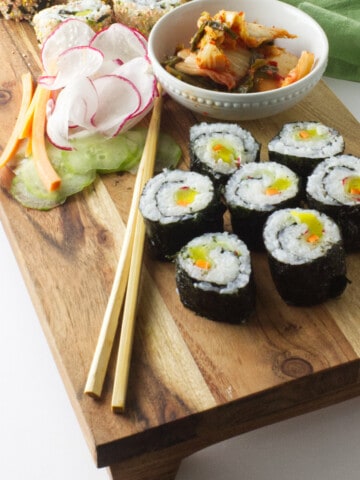 kimbap on a wood platter with chop sticks and kimchee.