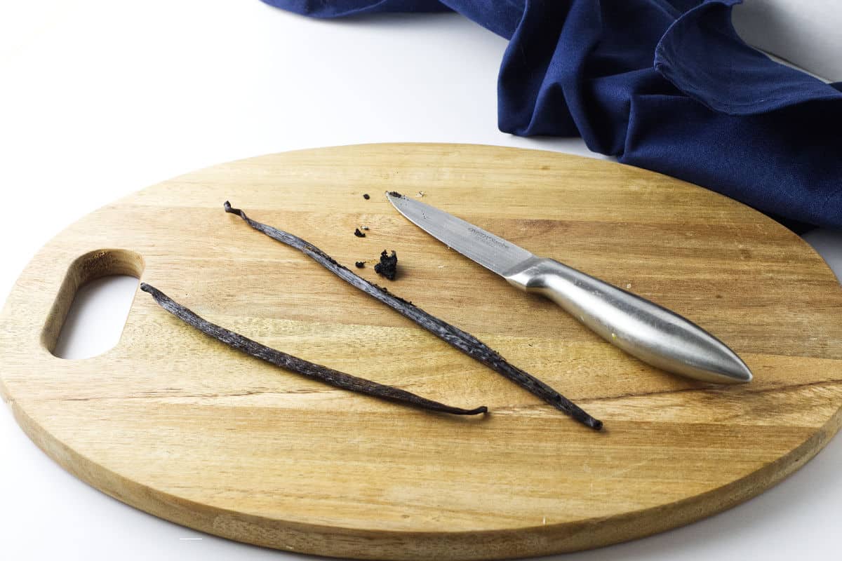 wood cutting board with stainless knife cutting a vanilla bean to extract caviar.
