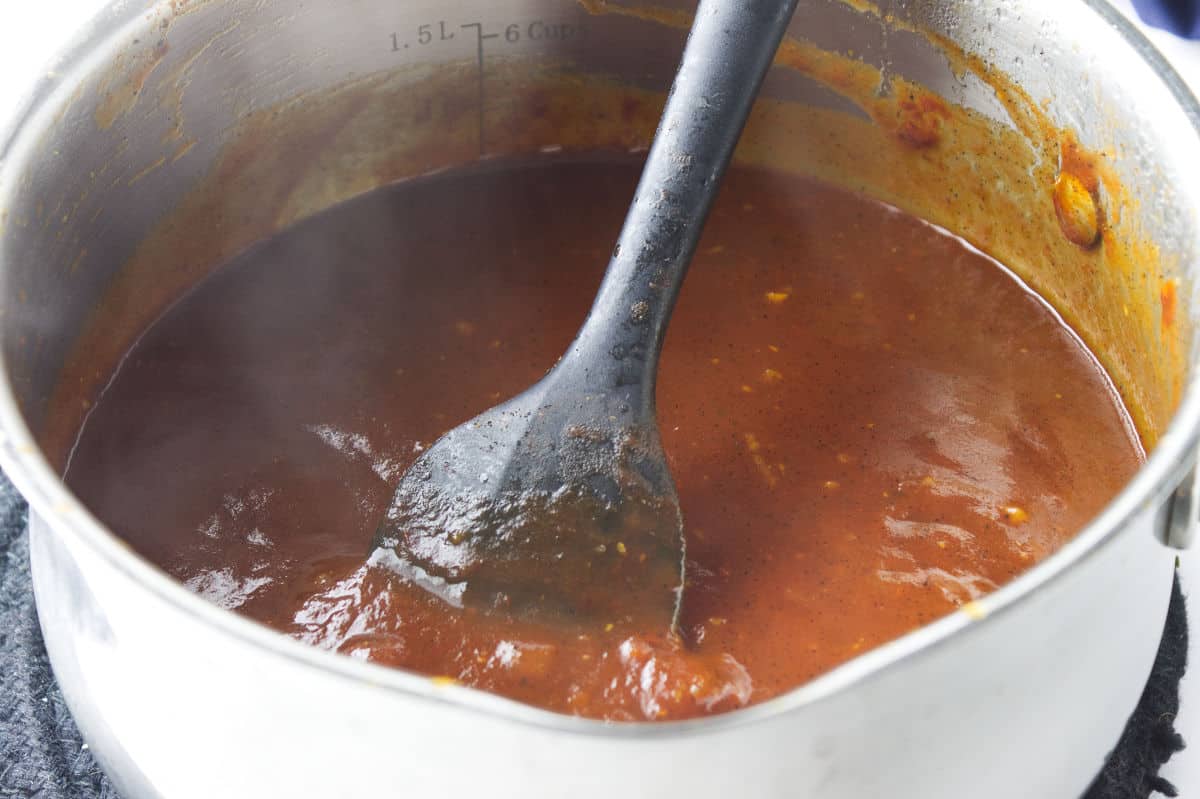 saucepan reducing barbecue sauce with steam rising and a black spatula stirring.