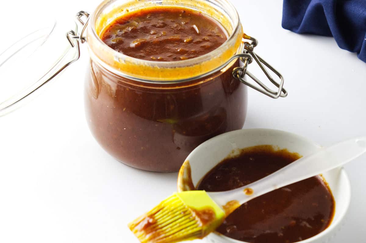 homemade barbeque sauce in a bail jar with basting brush and bowl of sauce.