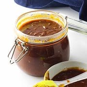 homemade barbeque sauce in a bail jar with basting brush and bowl of sauce on white background