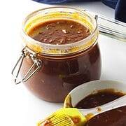 homemade barbeque sauce in a bail jar with basting brush and bowl of sauce on white background