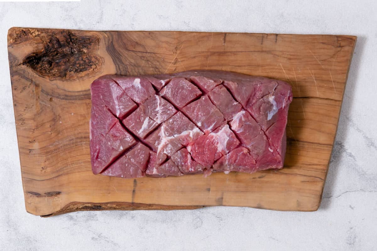 raw scored flat iron steak on wood cutting board.