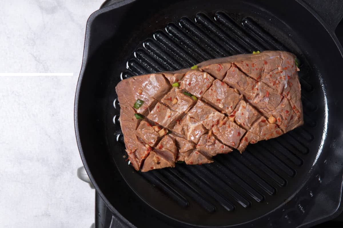 cast iron skillet with scored marinated raw flat iron steak.