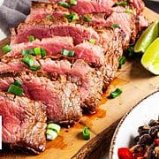 sliced flat iron steak on wooden plank with scallions, limes, and black bean salsa.