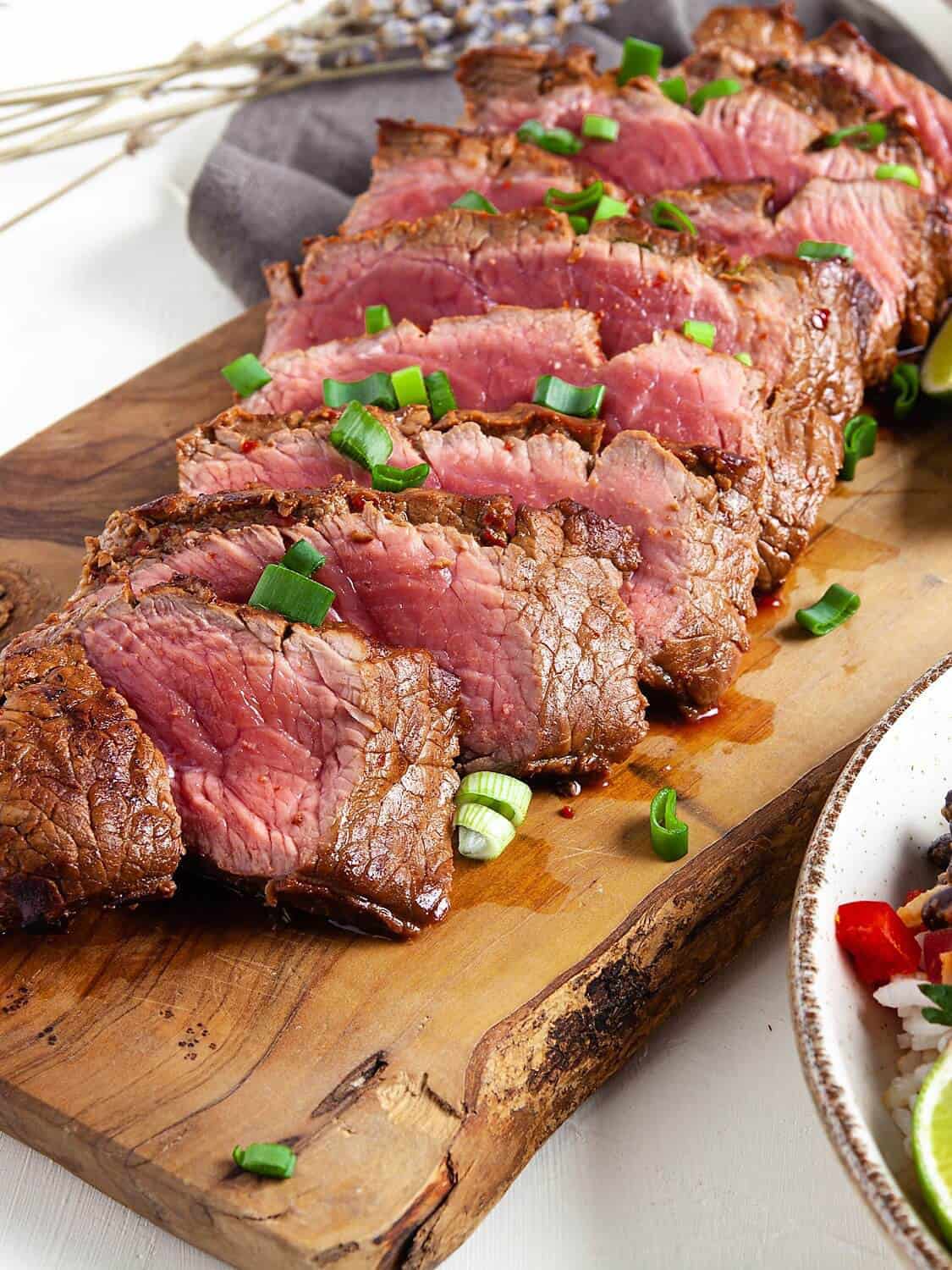 sliced rare flat iron steak on a wooden cutting board.