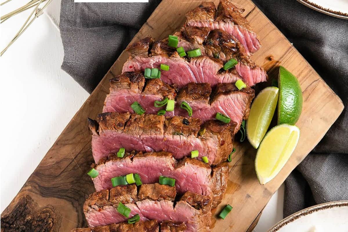 sliced grilled rare flat iron steak with sliced limes.