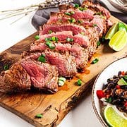 sliced flat iron steak on wooden plank with scallions & limes.