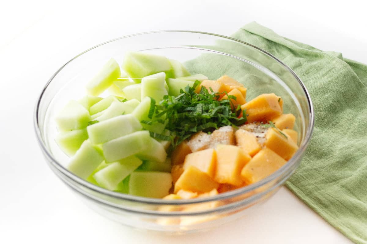 clear bowl with cut melon cubes, minced mint, and seasonings.