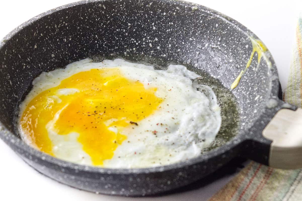 egg frying in a grey speckled skillet on a white background.