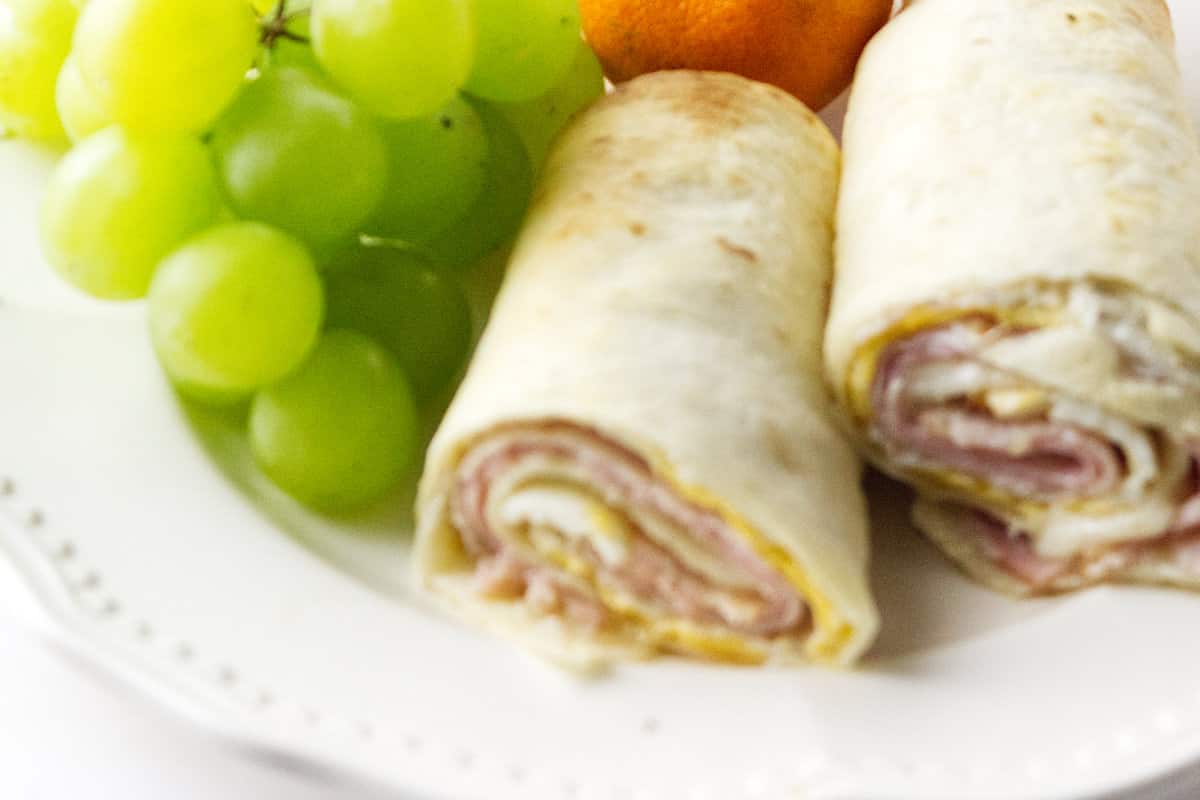 white plate with Monte Cristo Roll Ups, green grapes, and tangerine.