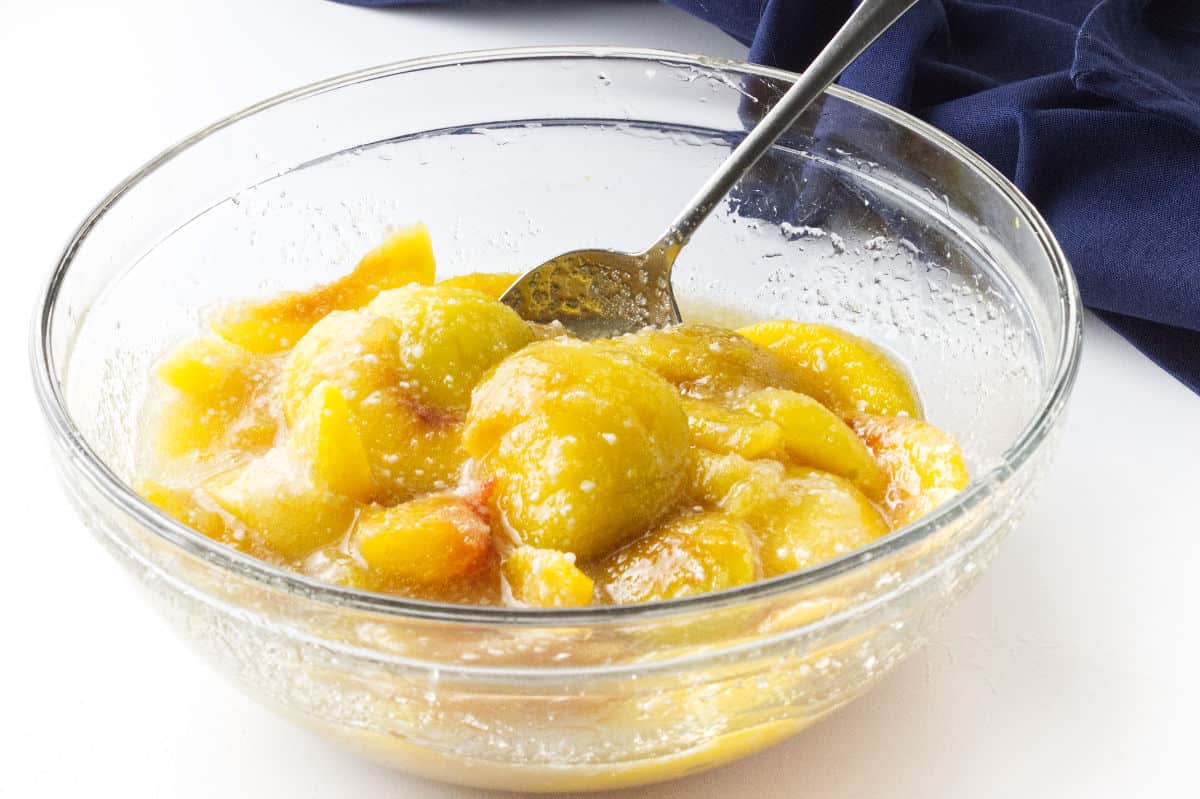 clear glass bowl of sliced peaches mixed with sugar for crumble filling.