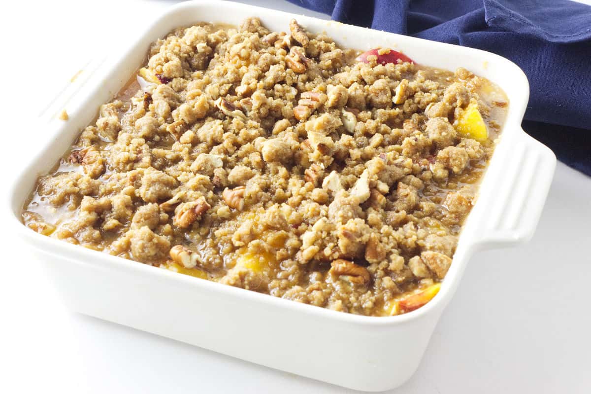 unbaked peach crumble in a white casserole dish.
