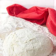ball of dough rising on a floured wood board with red towel in background