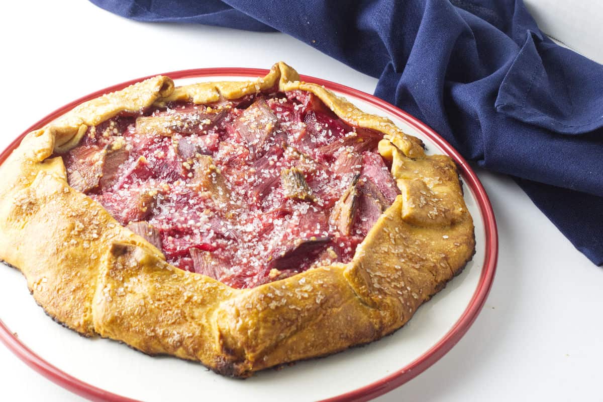red rimmed white cake plate with baked rhubarb gallette sprinkled with large grain sugar crystals.
